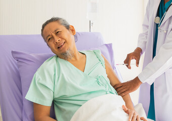 Elderly patient man sitting on bed unhappy, ache, sad, suffer from syringe in hand of doctor with stethoscope. Doctor or nurse take care senior patient health admission at hospital