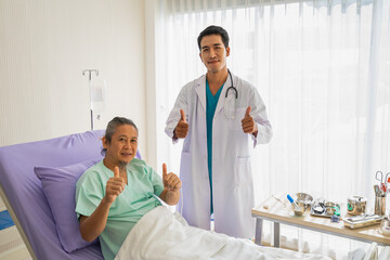 Fototapeta premium Elderly patient man with saline and doctor with stethoscope show thumbs up and happy to looking to camera. Doctor or nurse take care of senior patient health admission at hospital