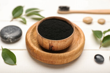 Bowl with activated charcoal tooth powder on white wooden background