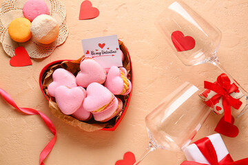 Box with tasty heart-shaped macaroons, greeting card, glasses and gifts on beige background