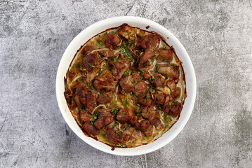Braised pork with onions  in a white baking dish on a dark grey background. Top view, flat lay