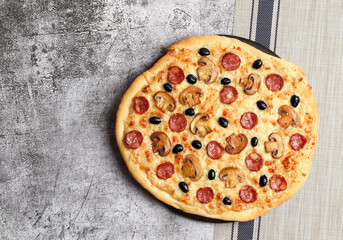 .Homemade Mushrooms Pizza with White sauce, mozzarella, olives and pepperoni on a round wooden cutting board on a dark grey background. Top view, flat lay