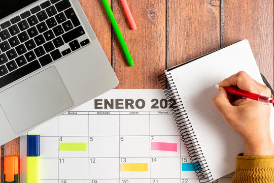 Person writing annotations of the activities to be carried out in a notebook together with a calendar in Spanish and his laptop. Concept of time organization and obtaining objectives. High quality