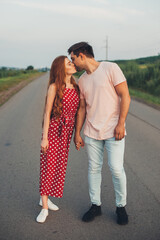 Full length of a passionate caucasian couple posing while golding hands and kissing on a road over picturesque landscape.