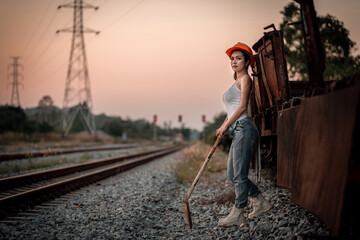 ฺBeautiful woman coal worker showed tried from work sitting on railway drinking water with orange helmet and shoveling coal relax after finished work.