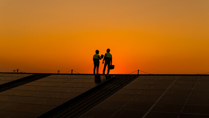 Engineers walking on roof inspect and check solar cell panel by hold equipment box and radio...