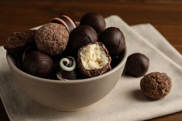 Bowl with many different delicious chocolate truffles on wooden table
