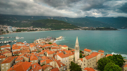 Naklejka na ściany i meble Aerial evening view of Budva old town with red rooftops and dramatic clouds, Montenegro