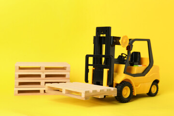 Toy forklift and wooden pallets on yellow background