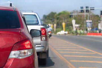 Traffic conditions on roads in Thailand. Red car parked at the end of a traffic light on an asphalt road. Turn on brake light. Traffic conditions during the clear daytime in the provinces.