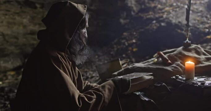 Aged sage man taking notes in book in cave