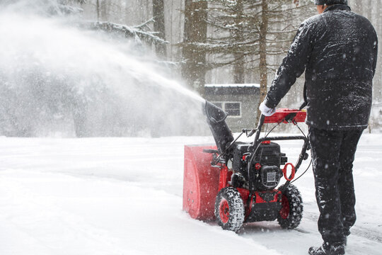 Man using snow blower machine to clear driveway at snow day.