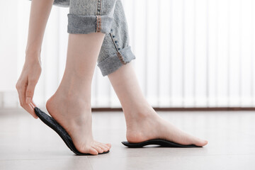 Woman fitting orthopedic insole indoors, close up. Girl holding an insole next to foot at home....