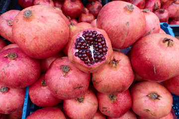Red ripe pomegranate fruits lie on display in a blue plastic box at a vegetable market. One pomegranate was peeled to show the ripeness of the grain. Selective focus.