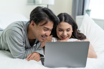 Asian attractive happy young couple watching movie on bed in bedroom. 