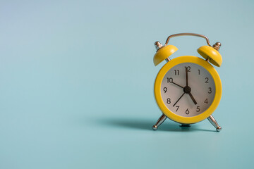 Yellow alarm clock with graduation cap on blue background closeup with copy space