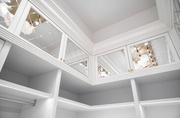 Fototapeta premium Luxury white walk-in closet with led lamps on shelves and mirror facades with rhombuses and contemporary luster in apartment