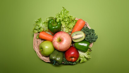 Top view organic vegetables and fruits in wicker basket on green background.