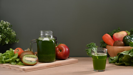 Homemade healthy green vegetable juice with ingredients on wooden table.