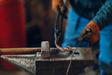 Blacksmith forges and making metal horseshoe with hammer and anvil at forge.