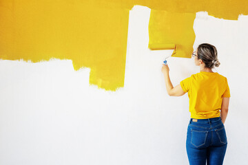 A woman in a yellow T-shirt is painting a wall in her house. Place for text