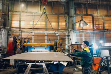 Worker lift metal sheet with crane chain hoist with remote controller and hook at industrial...