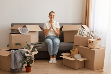 Portrait of happy optimistic woman wearing white casual T-shirt and jeans, sitting on sofa,...