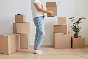 Portrait of unknown anonymous faceless woman wearing jeans moving new place, holding cardboard box with belongings, relocating, renting or buying new flat.