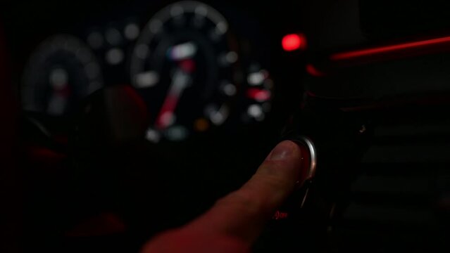 male driver finger press on red start engine button in sport car dashboard at night
