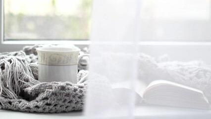 Cozy home with cup of coffee and a book. Hygge style. Mug of black coffee wrapped in warm scarf on wooden board. Top view, vintage style, Still life.