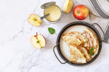 Celebrating Pancake day, healthy breakfast. Homemade sweet crepes with apples and condensed milk on a marble tabletop.  Top view flat lay. Copy space.