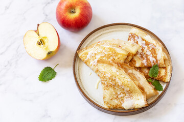 Celebrating Pancake day, healthy breakfast. Homemade sweet crepes with apples and condensed milk on a marble tabletop.