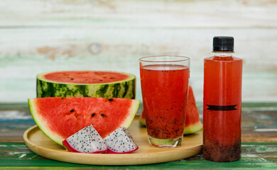 Close up studio shot of sweet delicious healthy sliced watermelon and fresh ripe cold dragon fruit juice in glass placed on wood plate and no brand bottle packaging for advertisement with copy space