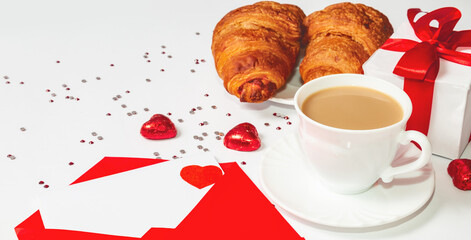 Cup of coffee, croissant and love letter, gift box on white table. Valentine's day breakfast