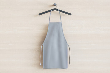Empty gray kitchen apron on hangers. Light wood background. Chef and cooking concept. Mock up...