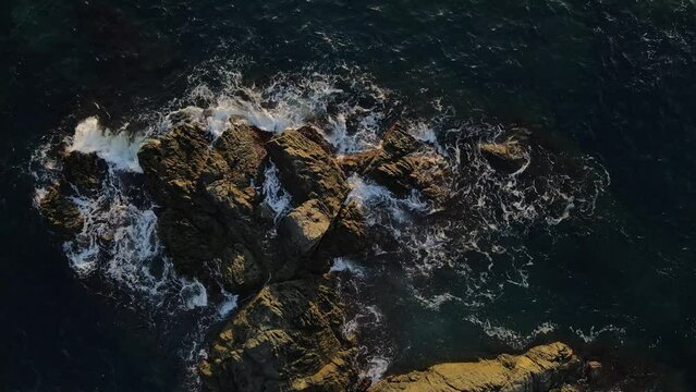 Ocean tide waves slam against rocks during sunset. Geological nature documentary-style footage.