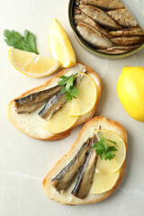 Sandwiches with sprats and ingredients on light background