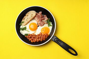 Pan with tasty breakfast on yellow background