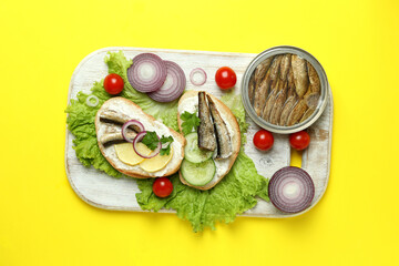 Board with sandwiches with sprats on yellow background