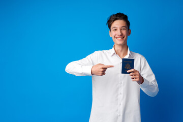 Portrait of glad handsome boy showing his passport going on vacation against blue background