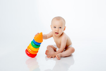 a little baby boy in a diaper is sitting on a white background playing a multi-colored pyramid , studio shooting