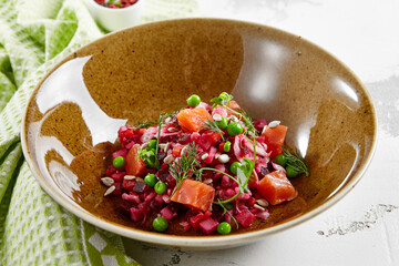 Traditional Russian salad - vinaigrette from boiled vegetables, cabbage and green pease. Vinaigrette salad with salmon in rustic style. Vegetarian dish in bowl on stone background. Russian food.