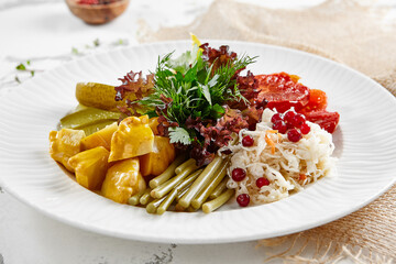 Appetizers from pickled vegetables in white stone background. Authentic food in restaurant menu. Mix from salted tomatoes, cucumber,  pickled pepper, sauerkraut. Assorted from marinated vegetables.