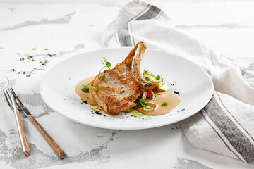 Roasted pork steak with vegetables garnish and sauce. Bone-in ribeye pork chops. Main course of pork in rustic style.