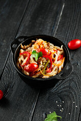 Japanese stir fryed udon noodles in wok. Udon noodle with beef and vegetables on wooden background. Asian noodles on black table with ingredients. Wok menu.