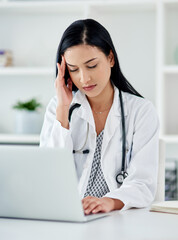 When the doctor needs a doctor. Shot of a young doctor looking stressed while using a laptop at her desk.