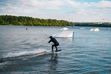 Wakeboarder sliding on water on board getting ready to perform ramp jump