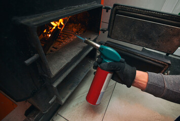 A man holds a gas burner and makes a fire in the solid fuel boiler in the boiler room. Solid fuel and heating concept