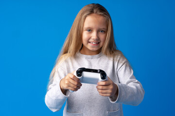 Young cute girl plays computer game with joystick on blue background