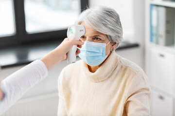 medicine, health and pandemic concept - doctor with infrared thermometer gun checking senior...
